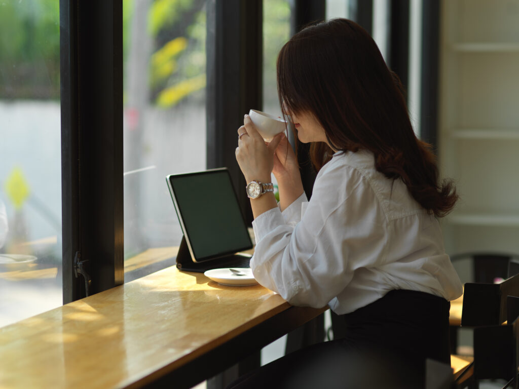 Side view of female freelancer drinking coffee while working with digital tablet in cafe